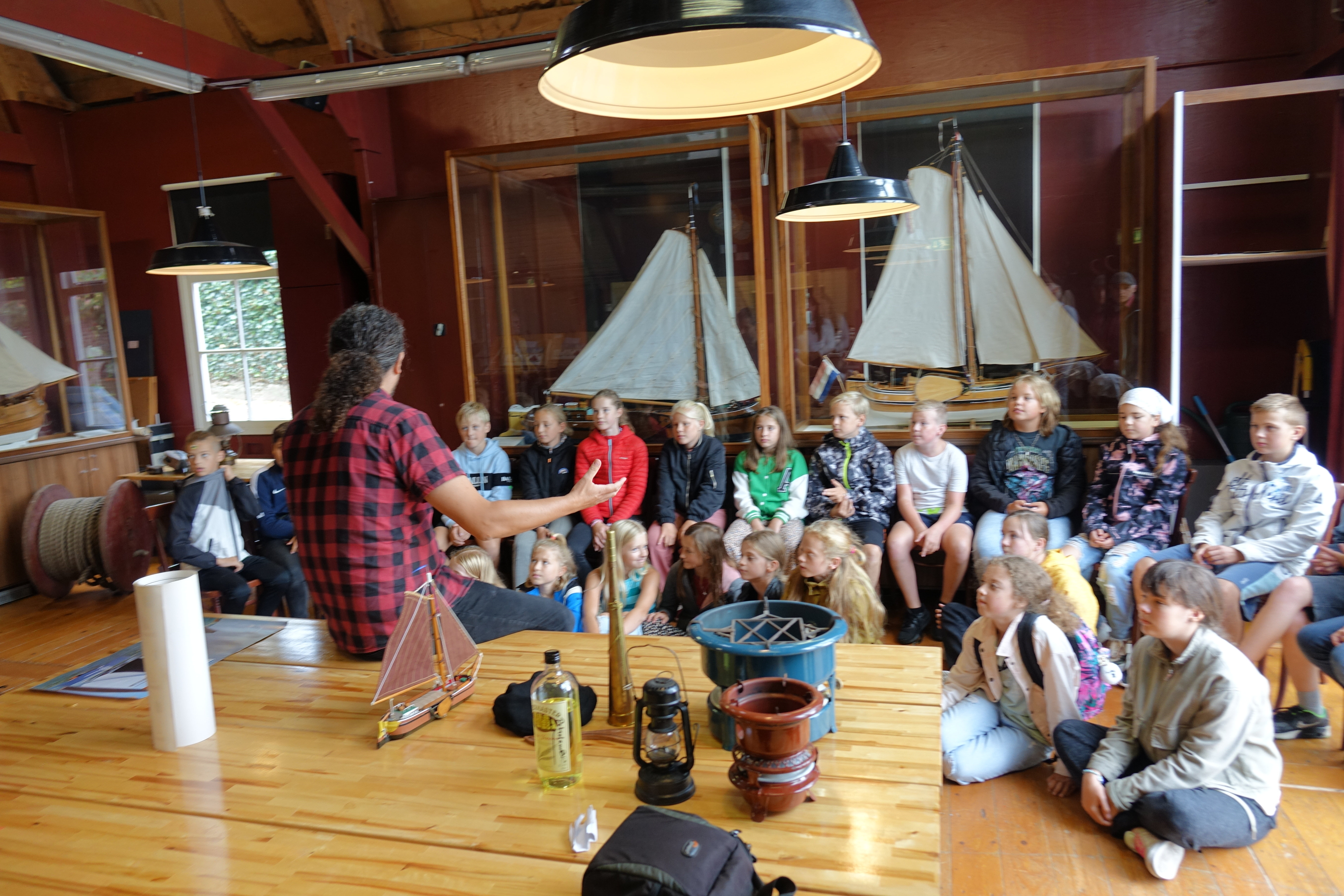 Kinderen luisteren naar uitleg in Museum Dokkum, met scheepsmodellen op de achtergrond